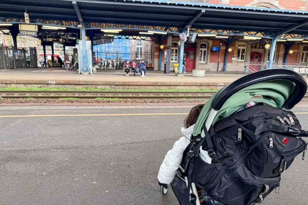 Babyzen Yoyo stroller at a train platform in Colmar, France with bags attached, showing how families manage baby travel stuff on intra-European rail trips.