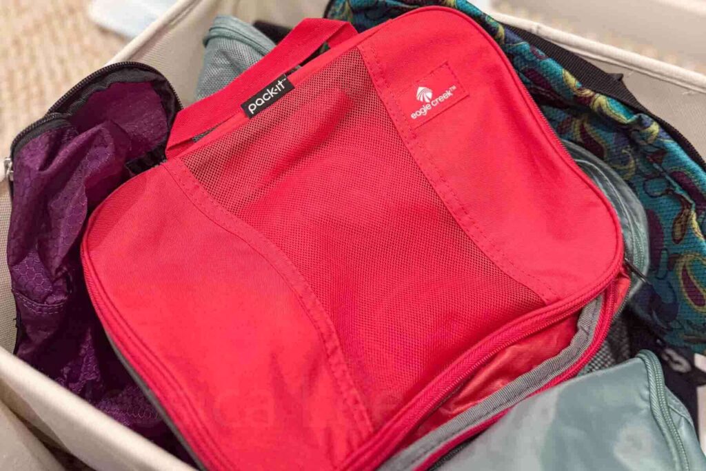 A high-quality red mesh Eagle Creek travel packing cube sits on top of a pile of other packing cubes.