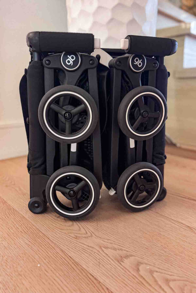 GB Pockit travel stroller folded, wheels tucked in, upright on a wooden floor, showing its ultra compact fold for comparison in gb pockit stroller vs yoyo discussions.