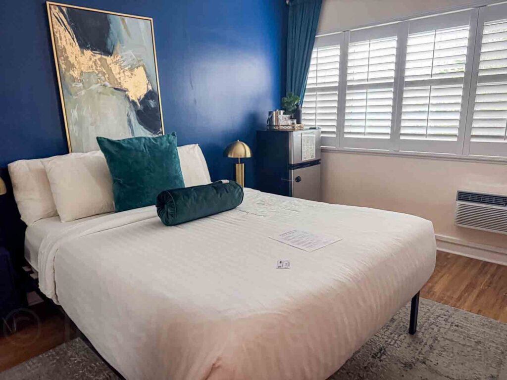 Hotel room at the Magical Castle Hotel in Los Angeles with a bold navy accent wall, gold lamp, and plush pillows 