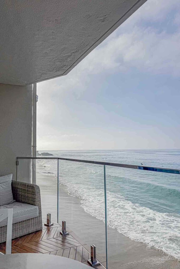Cozy oceanfront balcony with wicker seating and glass railing facing the shoreline. Ideal for couples looking for a relaxing staycation in Southern California. 
