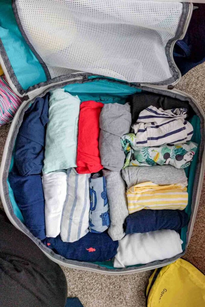 Rolled toddler clothes are packed snugly inside a bright blue packing cube with a mesh panel. The image shows packing tips for baby travel by keeping small clothing items together and easy to access.