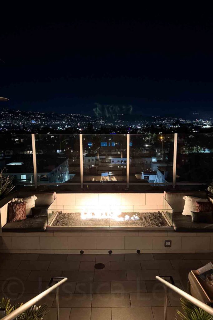 Rooftop fire pit with cushioned seating overlooking the city lights of Beverly Hills at night at the Kimpton Hotel Wilshire in Los Angeles