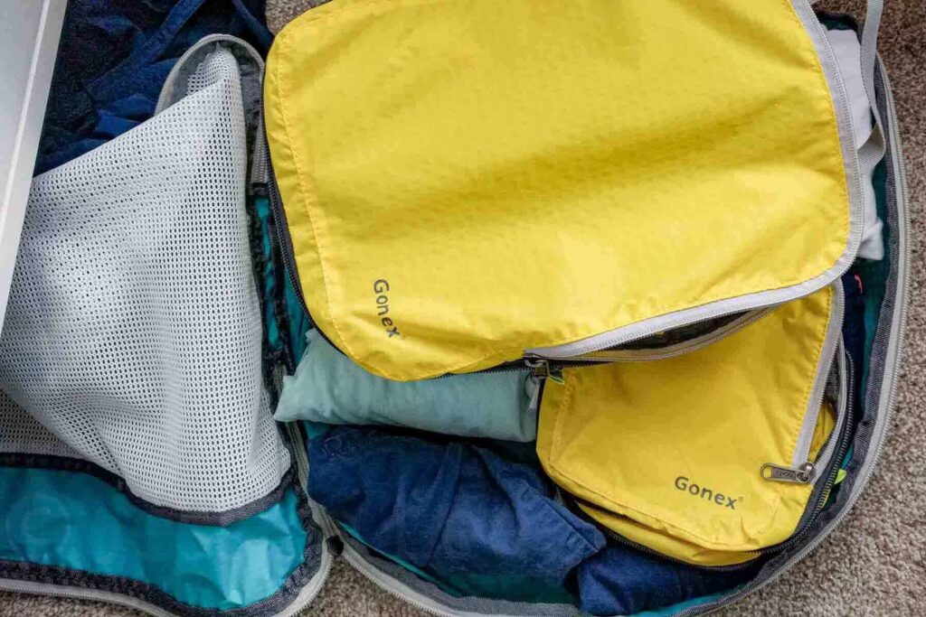A matching set of yellow Gonex packing cubes is set on top of another larger packing cube with clothing on the floor mid-packing. The image highlights one of the best packing cubes for families.