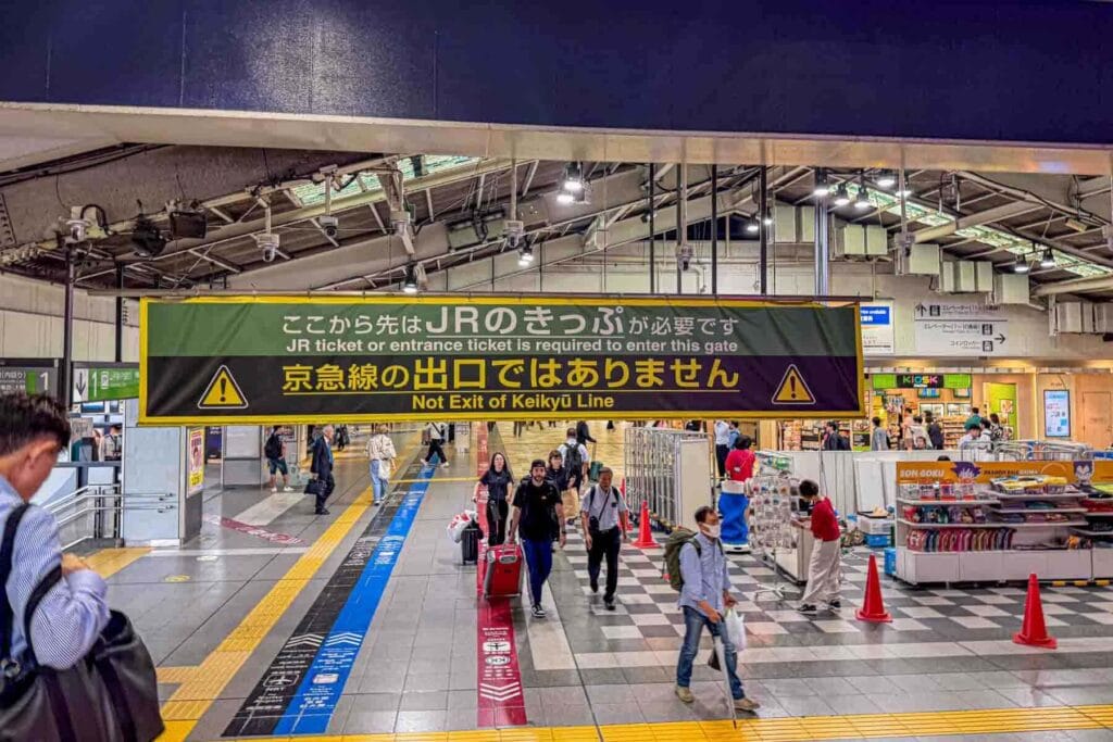 Busy Japanese train station with overhead sign reading JR ticket or entrance ticket is required and Not Exit of Keikyu Line. Clear station signage helps when navigating Japan.