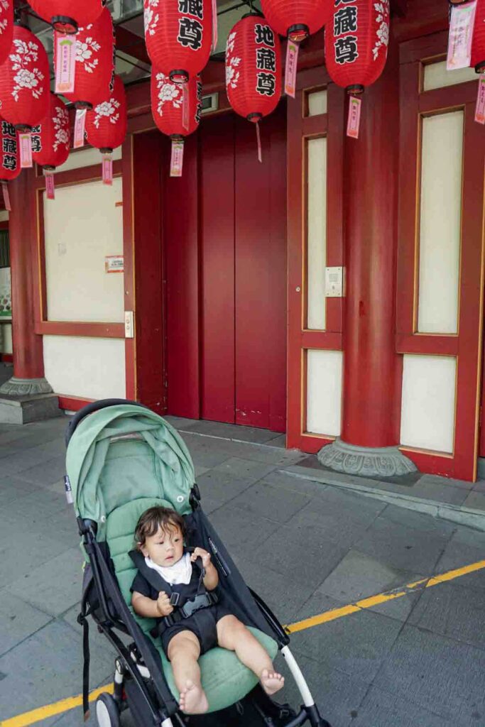 Seven month old baby sitting in a green Babyzen Yoyo stroller outside a temple in Singapore, showing sightseeing with a baby using one of the best travel strollers.