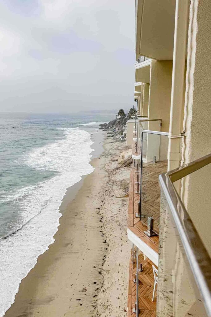 Angled view of a hotel balconies at Surf & Sand luxury hotel in Laguna Beach, California overlooking a serene beach with waves rolling in. A perfect view for a peaceful weekend getaway for parents.