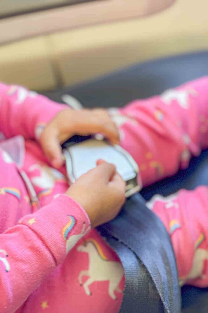 Close up of a toddler fastening an airplane seatbelt while wearing pink unicorn pajamas on a flight.