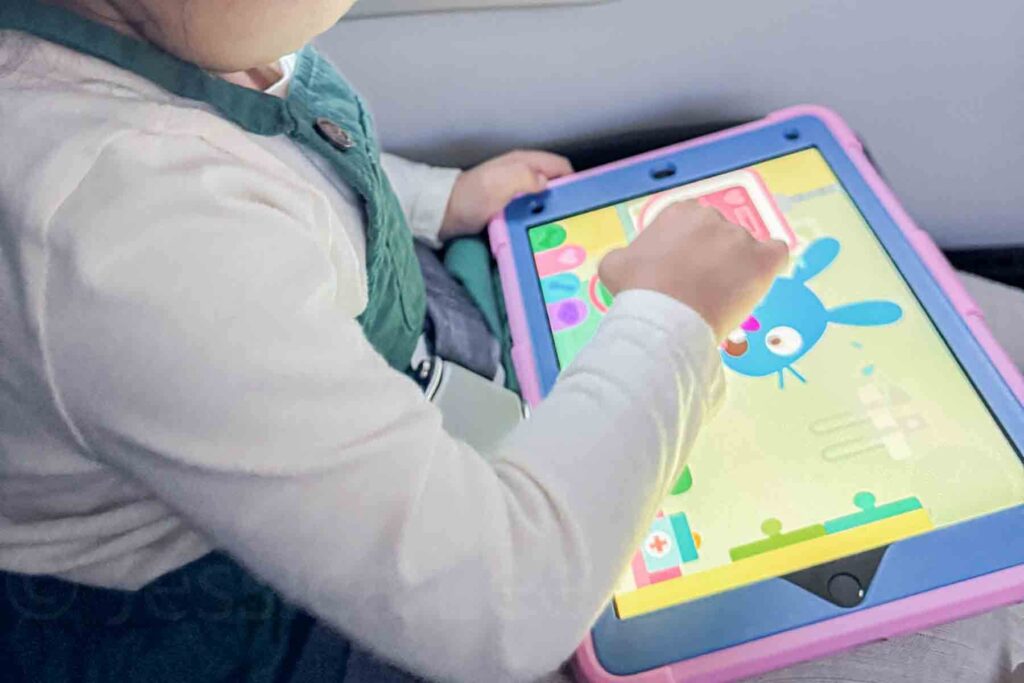 Toddler watching a colorful learning show on a tablet during a long flight, demonstrating a simple strategy for entertaining a toddler on a plane.