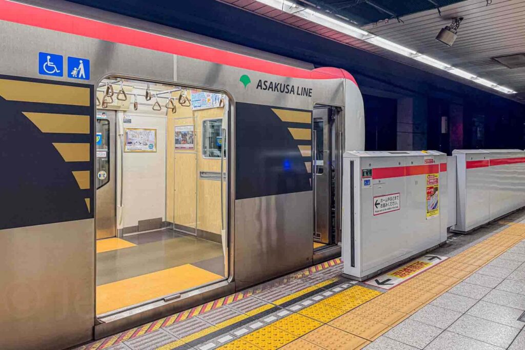 Asakusa Line train stopped at the platform in Tokyo, Japan with wheelchair and stroller priority symbols near the door. Demonstrates accessible public transport.