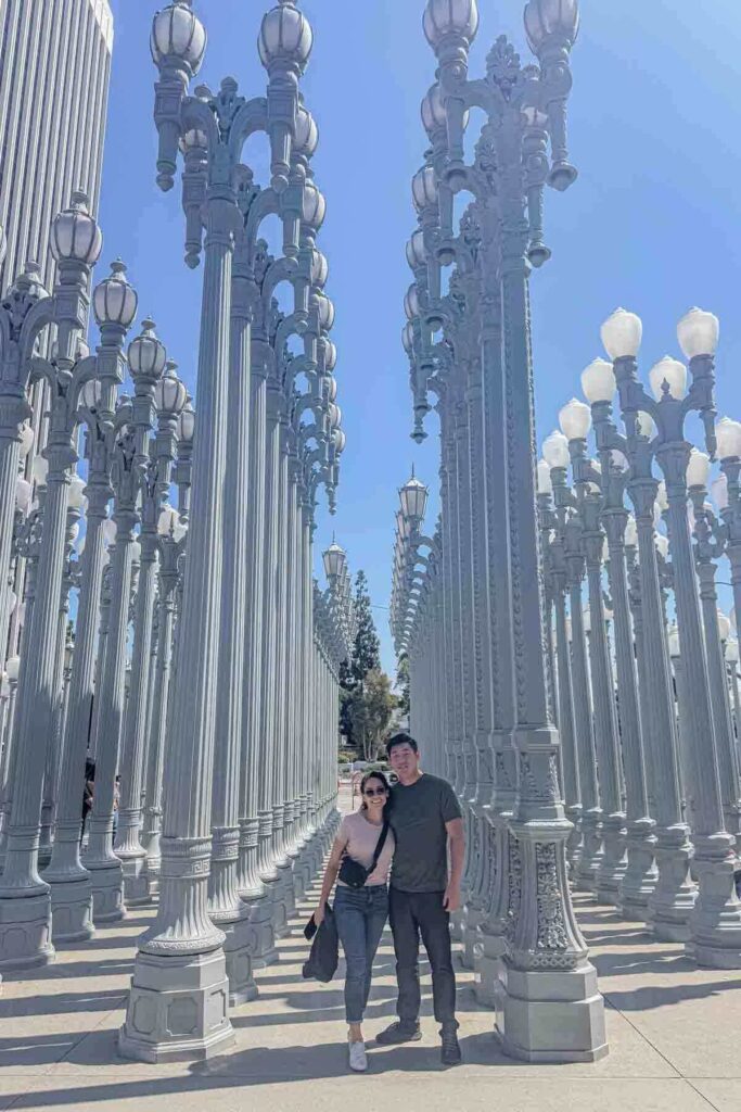 A couple poses together among the towering vintage street lamps at the Urban Light art installation at LACMA on a sunny day. The playful and iconic backdrop makes for a classic stop on a Los Angeles couple’s getaway.