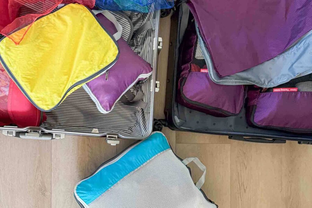 Image showing half of two open suitcases set on a wooden floor with yellow, blue, and purple packing cubes filled with clothing for a family trip.