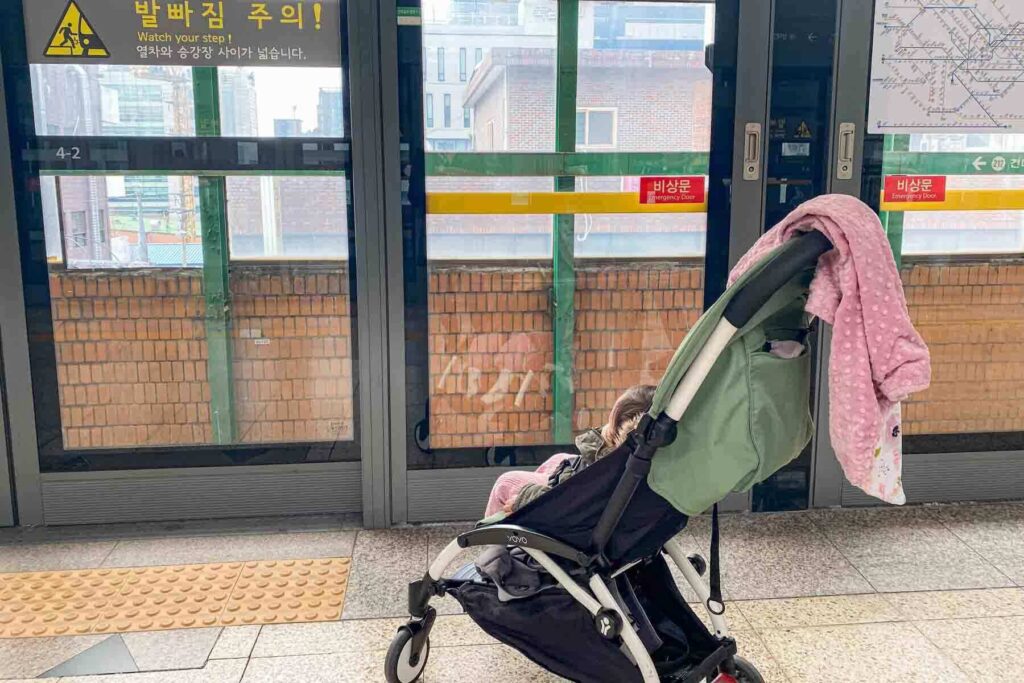 Young toddler riding in a Babyzen Yoyo stroller at a Seoul metro station, showing why travel strollers with a small footprint make traveling with kids easier