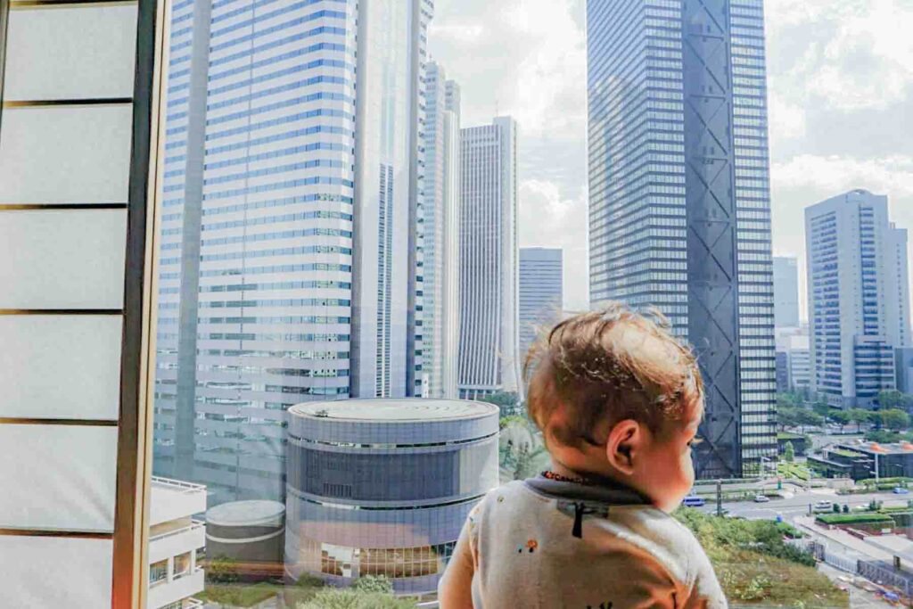 Baby looking out a hotel window at Tokyo skyscrapers and busy streets below. Views like this are common in some high-rise Tokyo hotels.