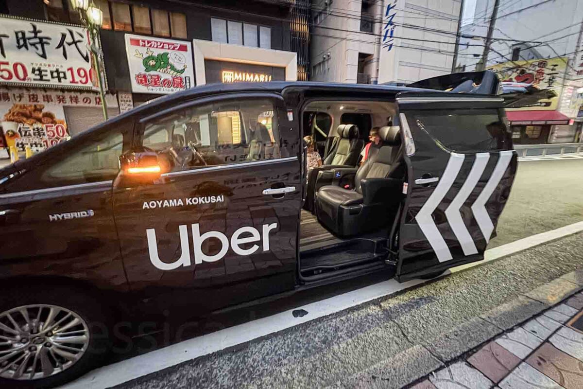 Black Uber minivan with sliding door open on a city street in Osaka as kids sit inside ready to ride. A practical option for getting around Japan with luggage and kids.