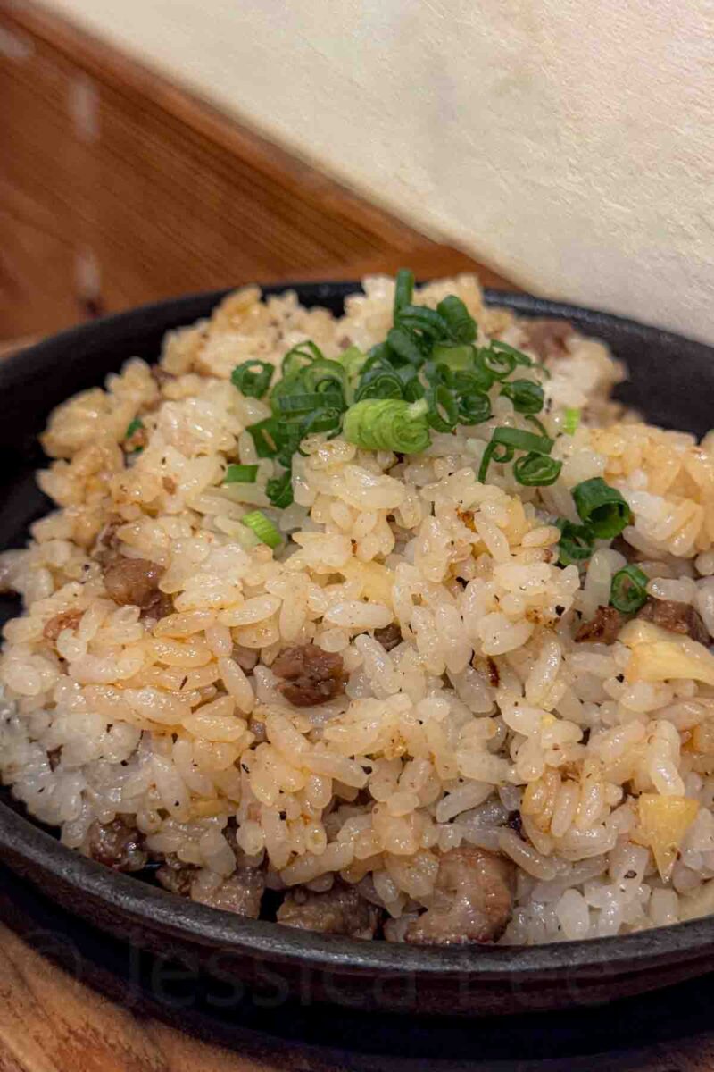 Close up of fried rice with small pieces of beef and chopped green onions in a dark black bowl. A familiar and easy meal choice for kids in Japan.
