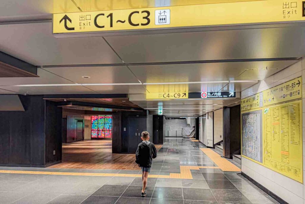 Child walking through a Tokyo metro station in Ginza under bright yellow exit signs. Easy train access like this helps families get around in Tokyo.