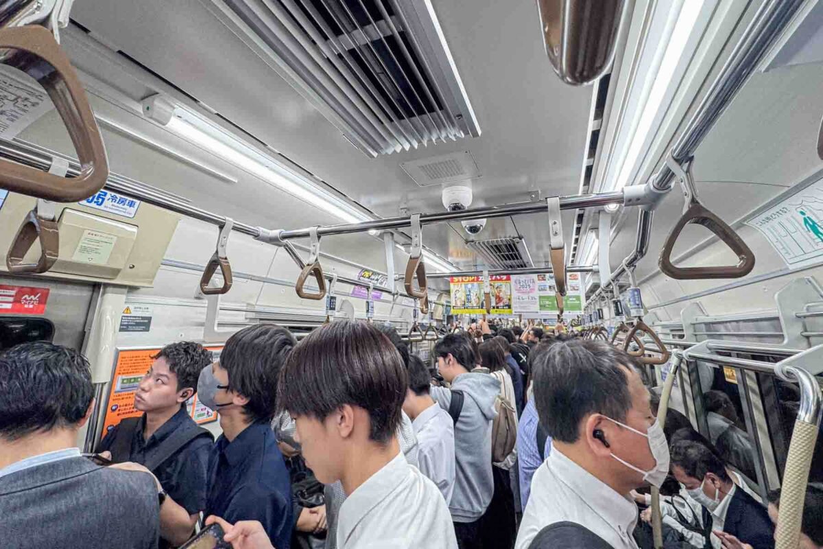 Crowded Tokyo subway car filled with standing commuters holding overhead straps during rush hour. Illustrates what to expect on busy trains when navigating Japan transportation with kids.