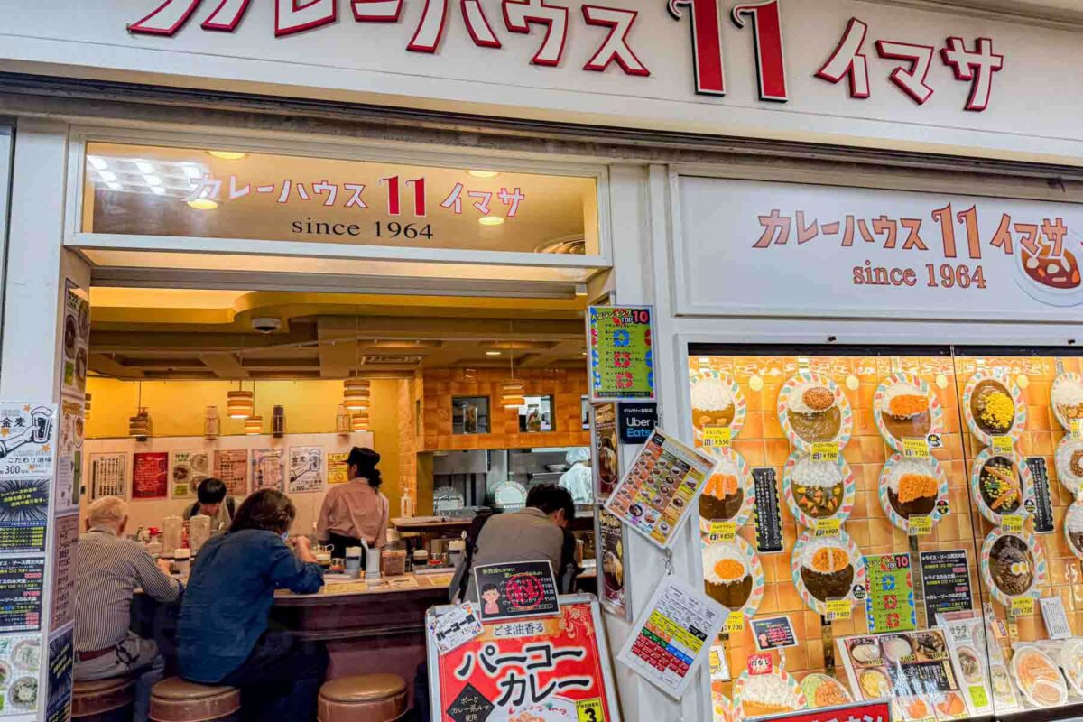 Small curry restaurant inside a busy train station in Shinjuku, Tokyo, Japan with diners seated at a counter and menu displays on the wall. Faux plates are displayed in the front window to show diners what to expect which can be helpful when traveling with kids.