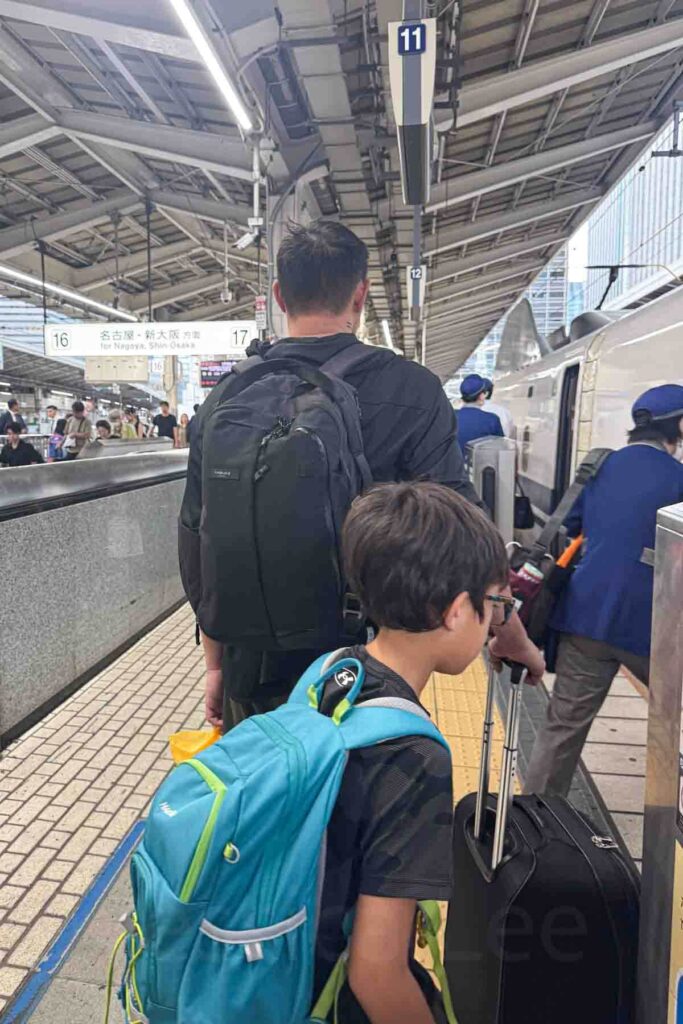 Father with a black backpack rolling luggage and child with a blue backpack while boarding a Shinkansen at Tokyo Station. Train travel like this is a core part of many Japan trips.