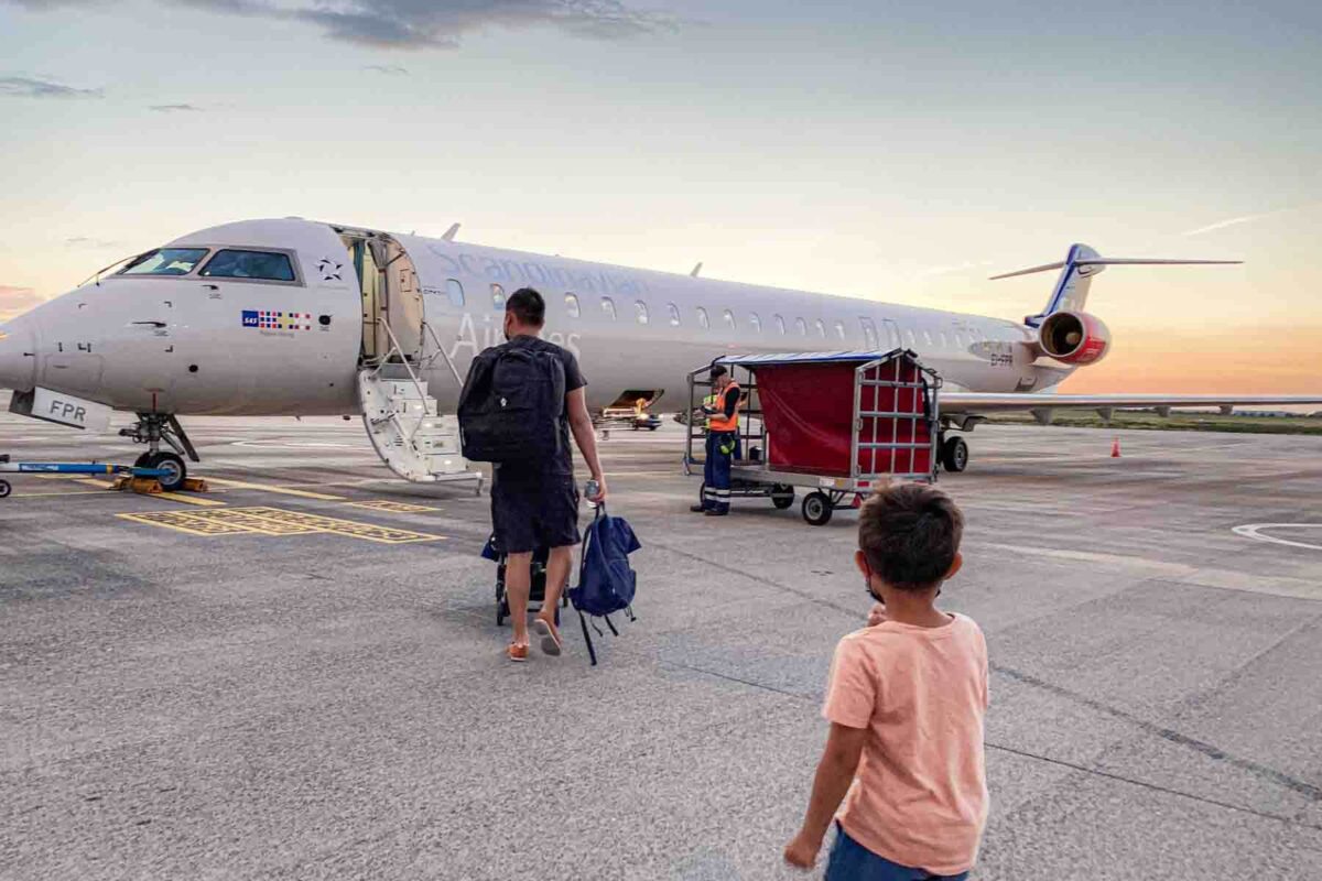 Dad walks across the tarmac with a travel stroller and backpacks while a child follows toward the Scandinavian Airlines plane during boarding for a flight.
