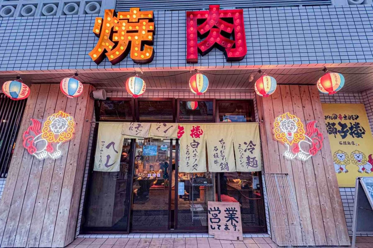 Restaurant facade with bold signage, bright neon-lit character lights, lanterns, and decorative lighting along the entrance. A casual and welcoming place for families to eat in Japan.