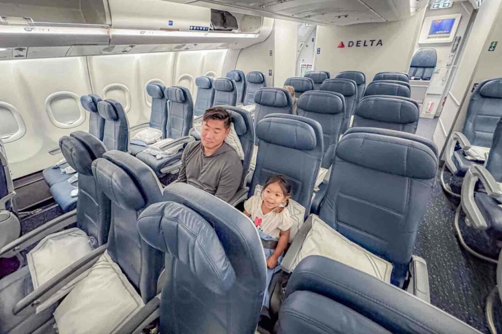 A father sits beside a toddler in the middle row of airplane seats with open space around them in the cabin on a Delta flight. The seating setup 2-3-2 shows how families with multiple kids can select their seats to have the best flight experience.