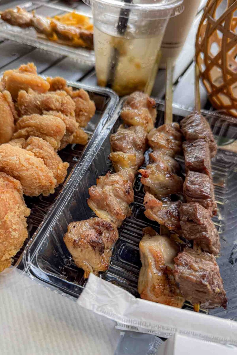 Open plastic takeout container of crispy fried chicken and grilled skewers with pieces of beef and chicken glazed and slightly charred. Street food style dishes that make eating in Japan with kids fun and varied.