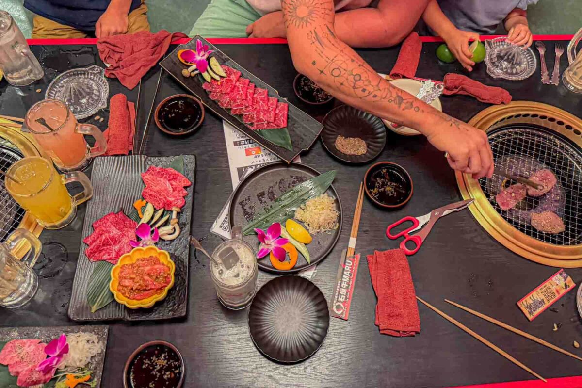 Plates of raw beef arranged beautifully with orchids and green leaves with vegetables and sauces around a tabletop grill at Ishigaki Beef MARU as diners cook together. A hands on meal that keeps kids involved while eating in Japan.