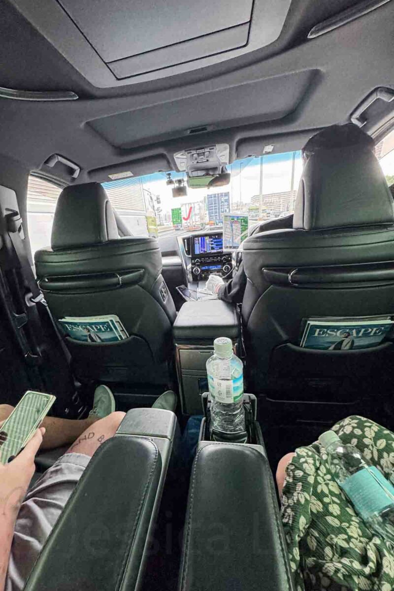 Interior of a spacious minivan in Japan with black leather seats and a center console as passengers ride in the back. A comfortable option for getting to and from the airport in Japan when traveling as a family group.