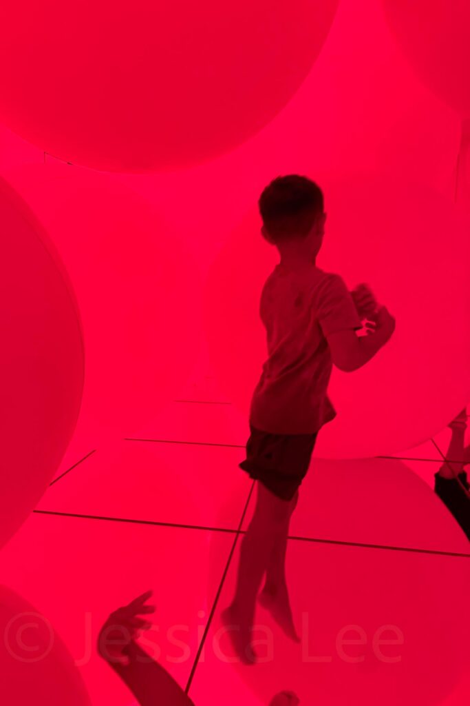 Child jumping among giant glowing red spheres in an immersive light installation room at TeamLab Planets. Play based exhibits like this are great for Japan with toddlers and older kids alike.