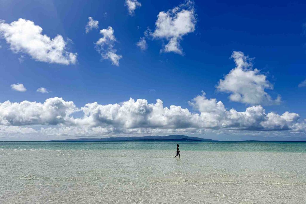Child walking alone through shallow crystal clear water at Kondoi Beach with distant islands on the horizon. Quiet beach stops show a different, often unexpected, side of a Japan trip.