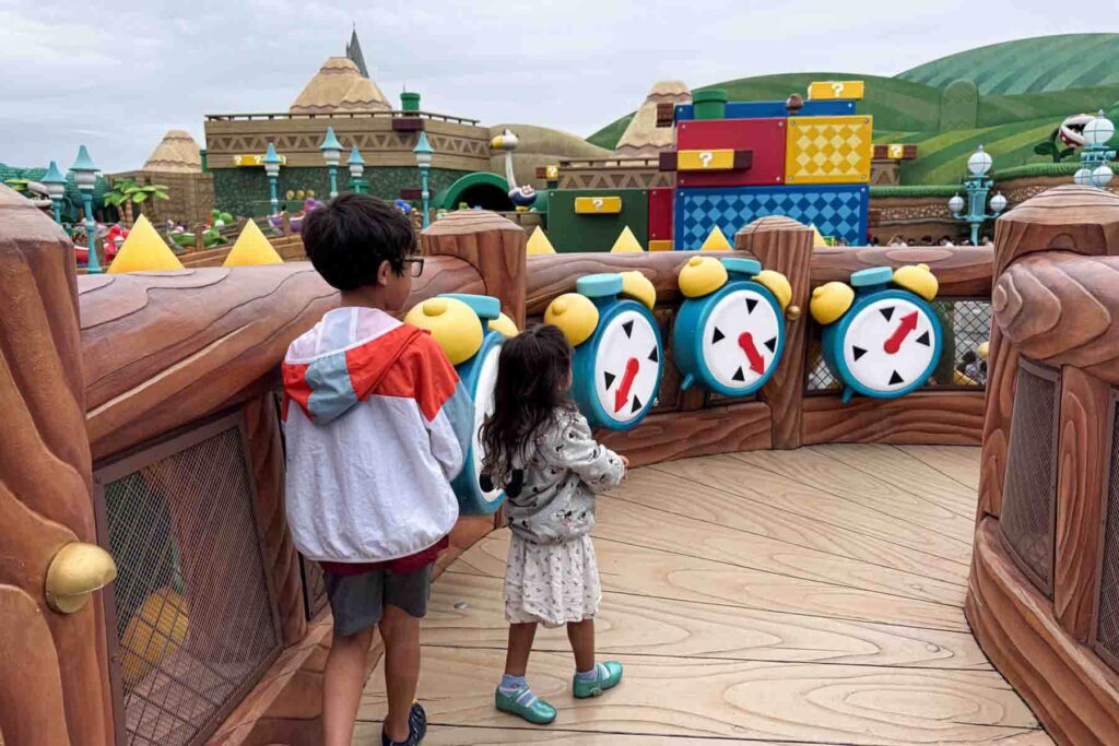 At Super Nintendo World in Universal Studios Japan, two children stand at an interactive game station with real-life cartoon-type alarm clocks and Mario world blocks in the background like they’re inside a video game. Theme parks like this are often a top reason families plan a trip to Japan with kids.