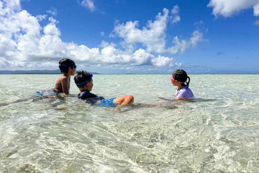 Three children floating and playing in clear shallow water at Kondoi Beach on Taketomi Island in Okinawa. Calm beaches like this are ideal for young swimmers.