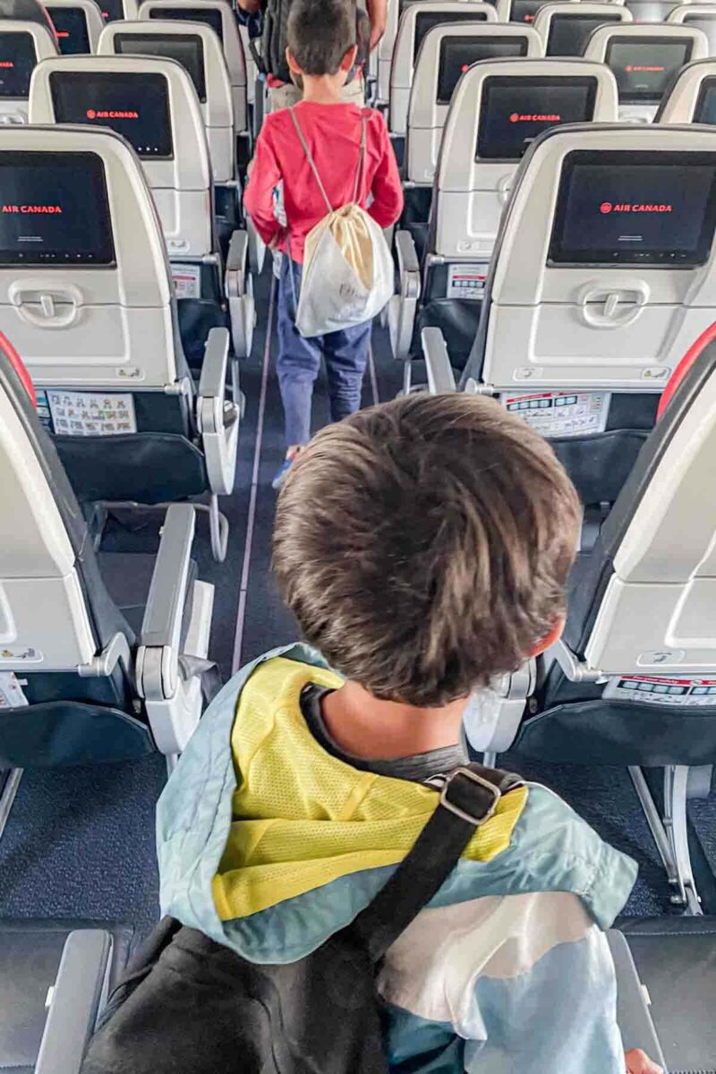 Two boys walk down the airplane aisle with screens showing "Air Canada" as they exit after a long flight.