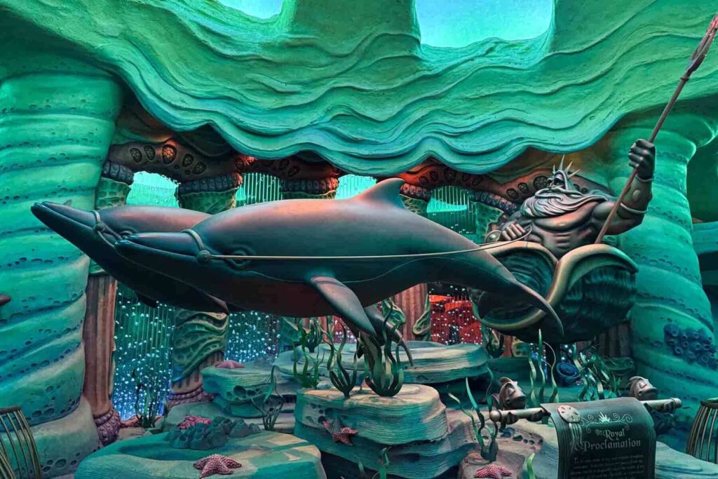 Large underwater themed statue of King Triton holding a trident beside sculpted dolphins in Mermaid Lagoon at Tokyo DisneySea. Themed play areas like this are especially fun for Japan with toddlers and mermaid lovers alike.