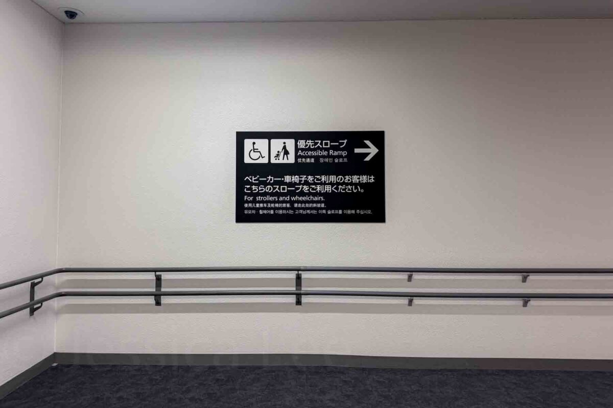 Wall sign with arrow reading "Accessible Ramp" and text "For strollers and wheelchairs" alongside accessibility icons. Highlights helpful infrastructure for getting around Japan.