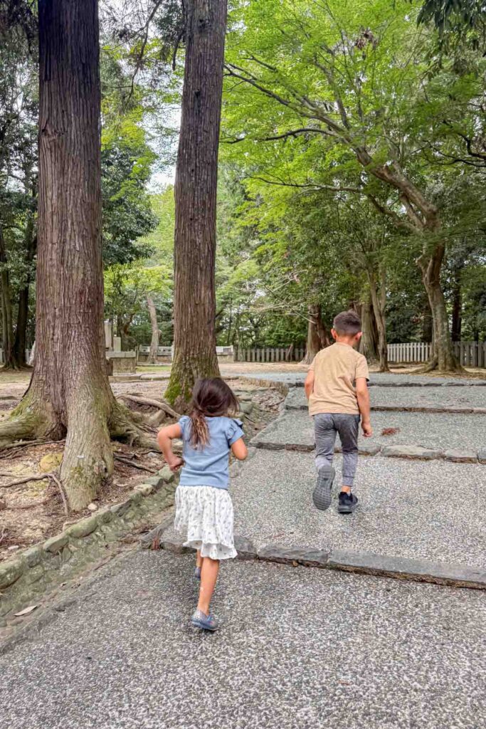 Two children walking up a stone path through tall trees at the Todai ji temple complex in Nara Park. Temple grounds like this can be a peaceful change of pace from the crowded streets and bright lights when traveling to Japan with kids.