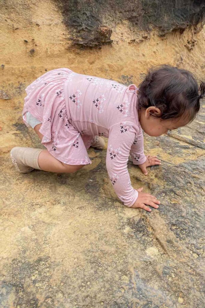 Toddler in a pink outfit crawls carefully over textured rock formations outdoors at a geopark in Taiwan. Her hands press against the uneven surface as she explores independently. Active stages like this can influence what is the best age to travel with a baby depending on how adventurous and mobile they are.