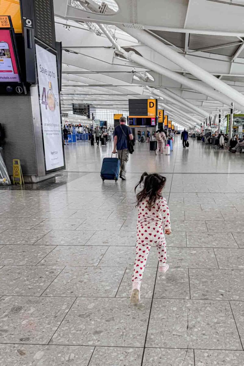 Toddler in heart pajamas runs through an airport terminal during check in for an international flight with kids.