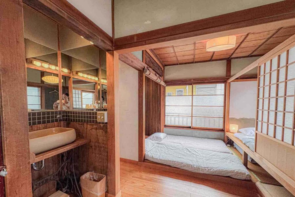 Interior of a traditional Tokyo townhouse with futon beds, wooden beams, sliding shoji doors, and a sink area. More spacious layouts like this can be helpful for larger families looking for accommodations in Tokyo.