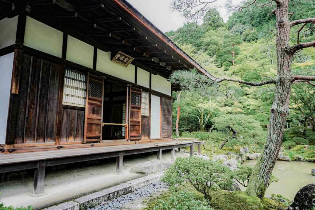Traditional dark wooden Japanese house with white panels with sliding wood doors opening onto a veranda beside a quiet garden and pond. Peaceful places like this balance busier days on a family trip to Japan.