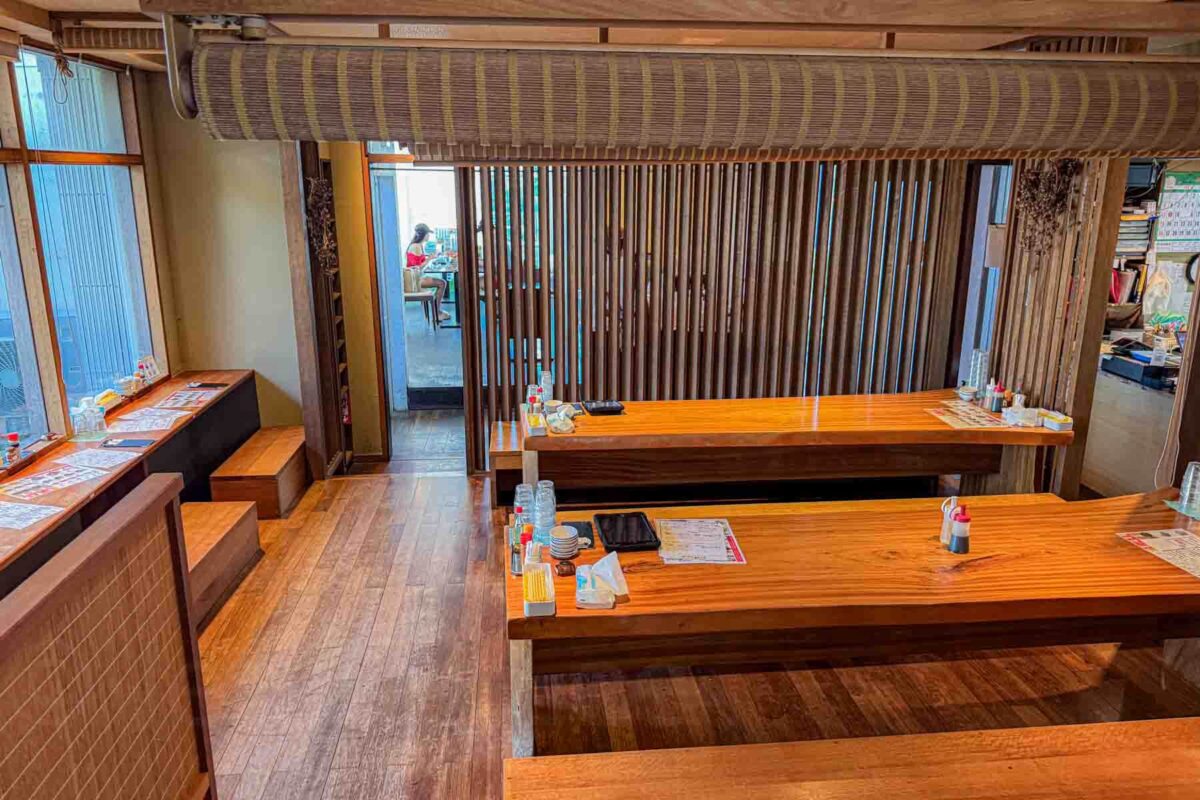 Traditional Japanese restaurant interior in Ishigaki with low wooden tables and bench seating arranged on a polished wood floor, with condiments and menus neatly set out. The spacious and calm layout shows a comfortable dining environment for eating in Japan with kids, especially for families needing more room.