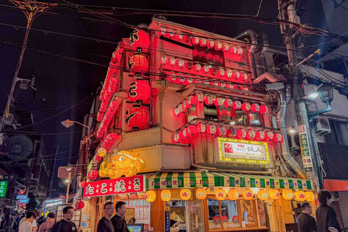Osaka street at night with a restaurant covered multiple levels of glowing red lanterns and bold signage. Bright lights and busy surroundings create an energetic dining atmosphere fun for families.