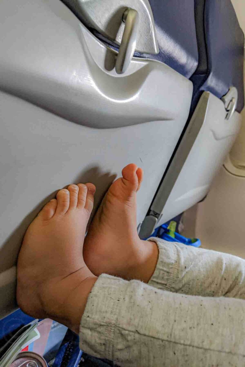 Baby’s bare feet resting against a closed airplane seatback tray, showing how simple movement and surroundings can help keep a baby occupied during a flight.