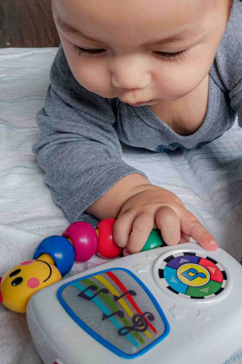 Baby pressing buttons on a Baby Einstein Take Along Tunes musical toy with colorful beads and notes, an engaging option to keep a baby busy on plane rides.