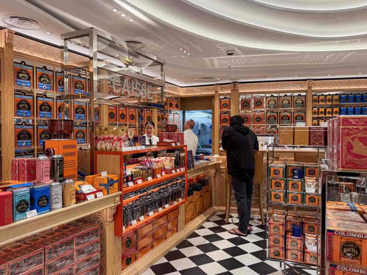 A richly decorated Bacha Coffee shop onboard displays rows of colorful coffee tins and packaged goods while guests browse the counter. This upscale cafe adds a unique dining and shopping element on the Disney Adventure cruise.