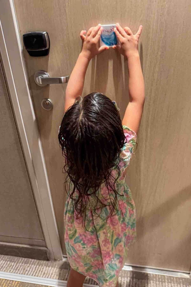 A child reaches up to place a magnet on a stateroom door, a popular way families personalize their space onboard. 