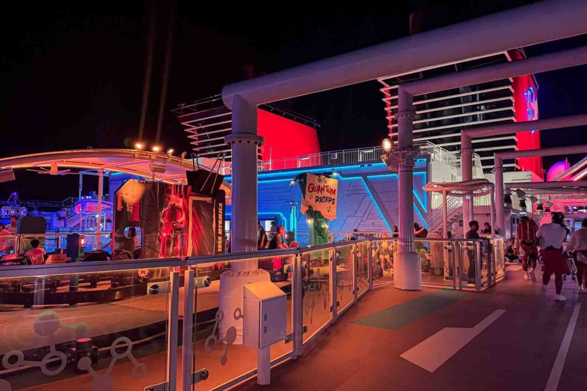 A neon lit deck at night features futuristic attractions and signage reading "Quantum Racers" surrounded by glowing blue and red lights. This scene captures the Marvel themed land area on the Disney Adventure cruise.