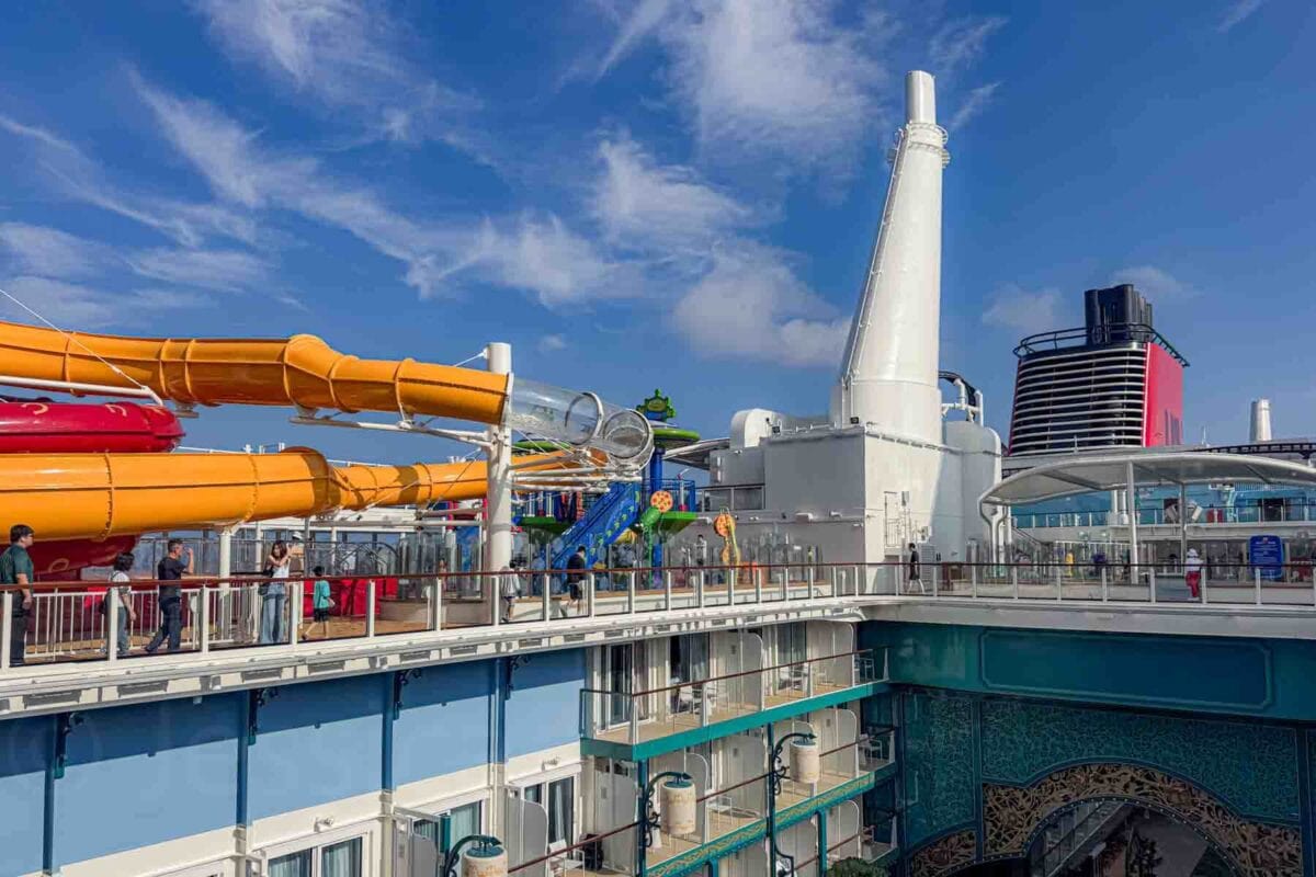 The upper deck features bright Toy Story themed water slides and play structures with guests walking nearby under a blue sky. This area showcases popular outdoor attractions and Disney cruise activities for kids onboard the Disney Adventure ship.
